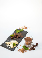 Fototapeta na wymiar Chunks of dark and white chocolate presented on a slate board with mint leaves on a white background.