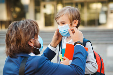 Father helping son and putting on face protective mask. Little boy going to school during coronavirus pandemic. Back to school 2020.