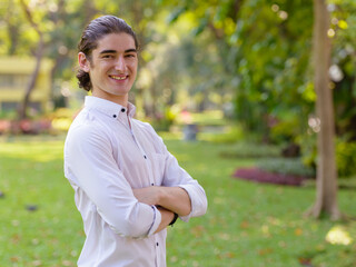 Happy young handsome businessman smiling with arms crossed at the park outdoors