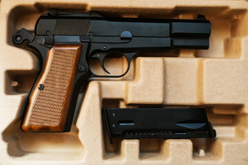 In a cardboard box is an airsoft gun with a brown handle, and next to it is a magazine. Sale and delivery of weapons.