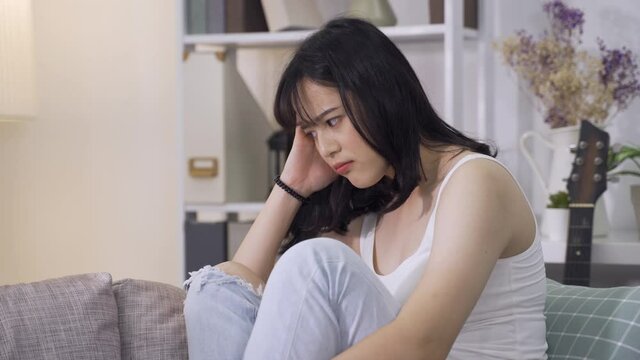 korean girl with worried look is filled with anxiety about the upcoming guitar performance. asian young lady huddling up on couch can’t get rid of obsessive thoughts about failing an important test.
