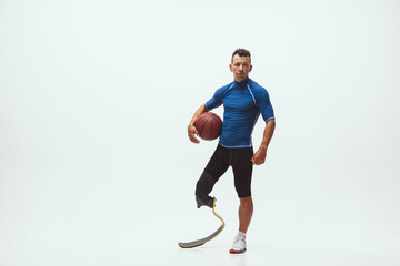 Fototapeta na wymiar Athlete with disabilities or amputee on white studio background. Professional male basketball player with leg prosthesis training in studio. Disabled sport and healthy lifestyle concept. Achievements.