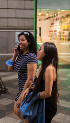 Young women walking around a square in the city while using their electronic devices