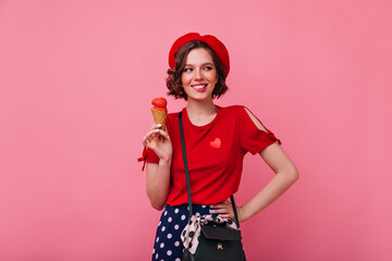 Enthusiastic young woman in trendy clothes eating ice cream. Indoor photo of smiling carefree lady with dessert.