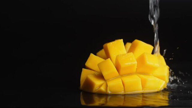 water with splashes pours on orange juicy diced mango on a black background. macro 180 fps
