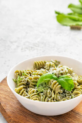 Green spiral pasta with sauce, grated cheese and basil in a white bowl on a concrete gray background. Free space for text. Cooked green girandole. Italian food.