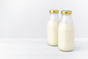 Two bottles of a fresh milk in a glass bottle with golden cap, oatmeal, almond, alternative natural drink. Healthy organic beverage close-up on a white table and light background, copy space.