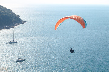 Paragliding in the sky. Paraglider tandem flying over the sea with blue water and mountains in...