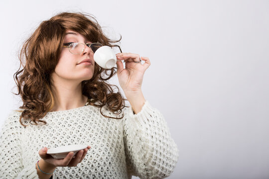 Signora con capelli mossi castani e maglione bianco beve il suo caffe da una tazzina , isolata su sfondo bianco 