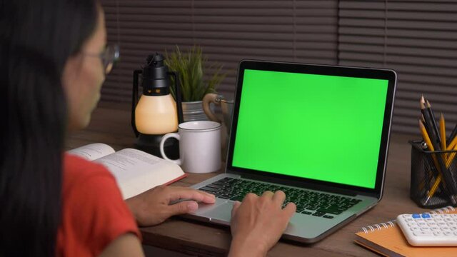 Over the shoulder shot of a business woman working in office interior on pc on desk, looking at green screen. Office person using laptop computer with laptop green screen, Dark Office.