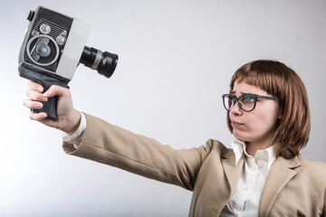 ragazza con capelli a caschetto e occhiali da vista si riprende cin una vecchia cinepresa da 8 mm, isolata su sfondo nero