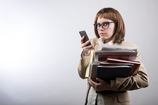 ragazza con capelli a caschetto castani , occhiali e abito tiene in mano un faldone di documenti e con l'altra utilizza il suo smartphone con aria seria , isolata su sfondo bianco