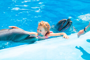 Happy little girl swimming with dolphins in Dolphinarium