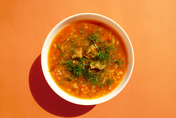 Kharcho soup in a white bowl on a bright orange background. Top view. Famous traditional Georgian kharcho soup with beef, rice and tomatoes. Georgian lamb and rice soup