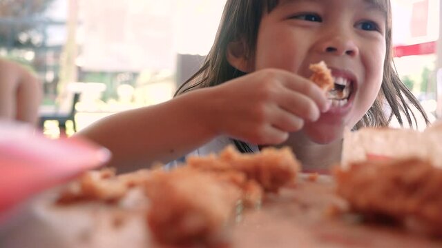 Happy child girl enjoy with eating fried chicken and French fries in service shop. Junk food and Health concepts.