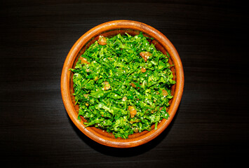 Famous traditional Arabic cuisine. Tabbouleh green salad in a brow on dark wooden background. Top view. Tabboula - levantine vegetarian salad with chopped parsley, mint, bulgur, tomatoes, lemon juice.
