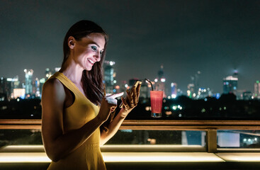 Naklejka na ściany i meble Beautiful woman checking her phone in rooftop bar