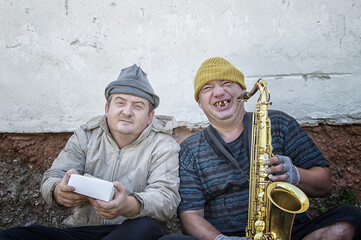 Homeless street musicians sit on the street with a saxophone and a donation box.