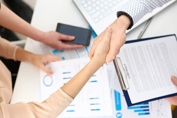 Kind male person standing opposite his partner and shaking hands after taking agreement during meeting