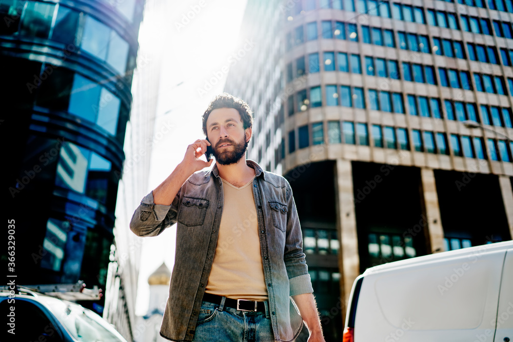Poster bearded hipster guy dressed in casual wear calling on smartphone and using high speed roaming connec