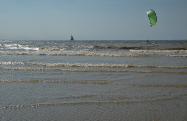 Ein Surfer in rote Oberkleidung mit einem grünen Segel ist am windsurfen über die Wellen des...