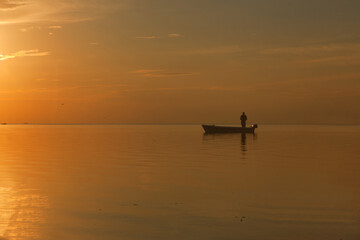 fisherman at the boat on golden sunset sea. beautiful and romantic sunset. silhouette of fishermen with his boat