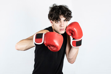 Athletic teenager trains in boxing gloves, practices side kicks, the guy has a passionate face, it...