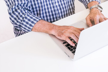 Senior man in plaid shirt typing on a gray laptop.