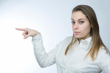 ragazza bionda con camicia bianca indica con aria stupita, isolata su sfondo chiaro