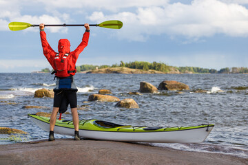 Happy man with a yellow sea kayak on the shore of a beautiful sea with raging surf. Evening time,...