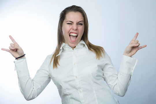 ragazza bionda con camicia bianca fa il segno delle corna con le mani come se fosse un rapper, isolata su sfondo chiaro