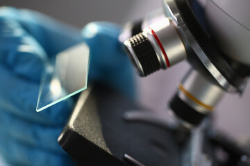 Professional researcher wearing rubber gloves while doing chemical research and using lenses of microscope