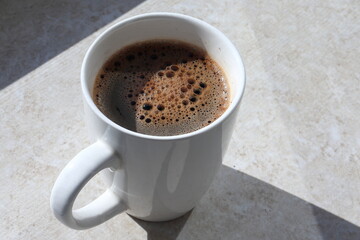 White cup of hot coffee on the table. Sunny morning. Close up view. 