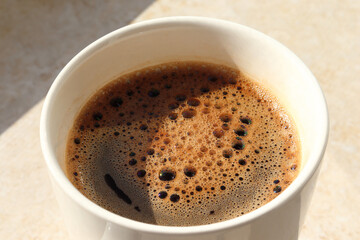 White cup of hot coffee on the table. Sunny morning. Close up view. 