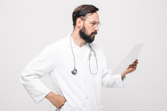 young serious male doctor in uniform with stethoscope reading medical document
