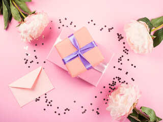 Stack of pink gift boxes with purple ribbon on pink background with peonies and envelope. Wedding, mother, womens day