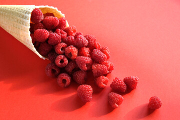 Fresh ripe raspberries in a waffle cone on a red background.