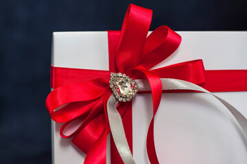 The gift box is white with a beautiful red bow. Gift on a dark background. Holidays and surprises....