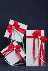The gift box is white with a beautiful red bow. Gift on a dark background. Holidays and surprises. Satin bows with rhinestones.