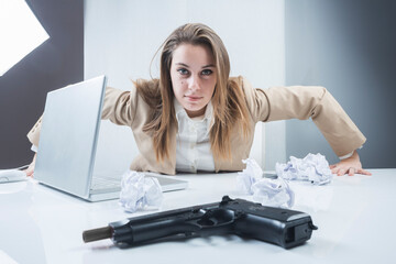 ragazza bionda vestita con una giacca beige è seduta nella sua postazione di lavoro e sbatte le mani sulla scrivania con una pistola in primo piano