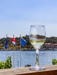 Croatia, Dalmatia, Makarska. A glass of white wine on the counter of an open restaurant with a view of the sea, seaside houses and flags of Croatia. Summer vacation in a Mediterranean resort