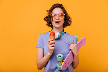 Portrait of smiling white girl holding longboard and eating dessert. Studio shot of brunette...