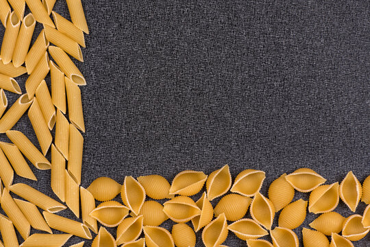 Conchilioni and penne rigate on gray background. Textured background culinary theme.