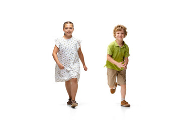 Fototapeta premium Happy children, little and emotional caucasian girl and boy jumping and running isolated on white background. Looks happy, cheerful, sincere. Copyspace for ad. Childhood, education, happiness concept.