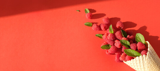 Fresh ripe raspberries and mint leaves in a waffle cone on a red background.