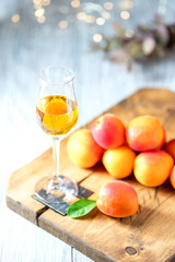 Apricot liqueur in shot glass and fresh apricots on a light wooden table in holiday colorful bokeh.