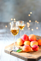 Apricot liqueur in shot glass and fresh apricots on a light wooden table in holiday colorful bokeh.