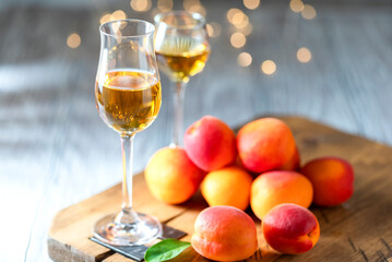 Apricot liqueur in shot glass and fresh apricots on a light wooden table in holiday colorful bokeh.