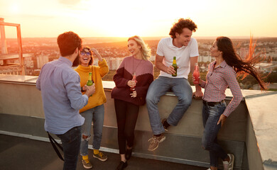 Cheerful young friends with drinks having party on rooftop