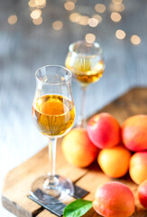 Apricot liqueur in shot glass and fresh apricots on a light wooden table in holiday colorful bokeh.